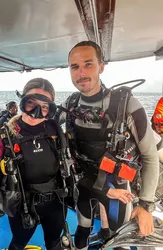 Two divers in wetsuits and scuba gear smiling together on a dive boat.