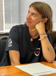 Smiling woman in an SSI t-shirt sitting at a desk with a dive log book, resting her chin on her hand.